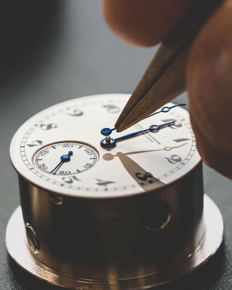 Watchmaker using tweezers to place hands on a watch dial.