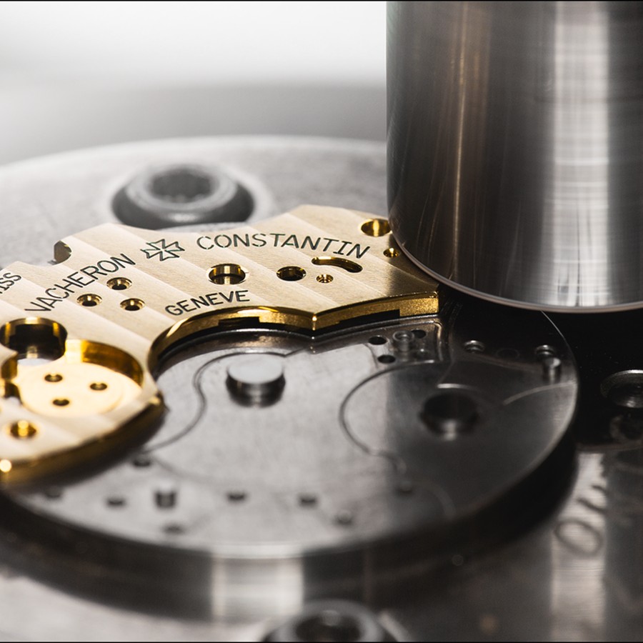 Detailed view of a Vacheron Constantin watch movement plate with engraved markings, positioned under a machine.