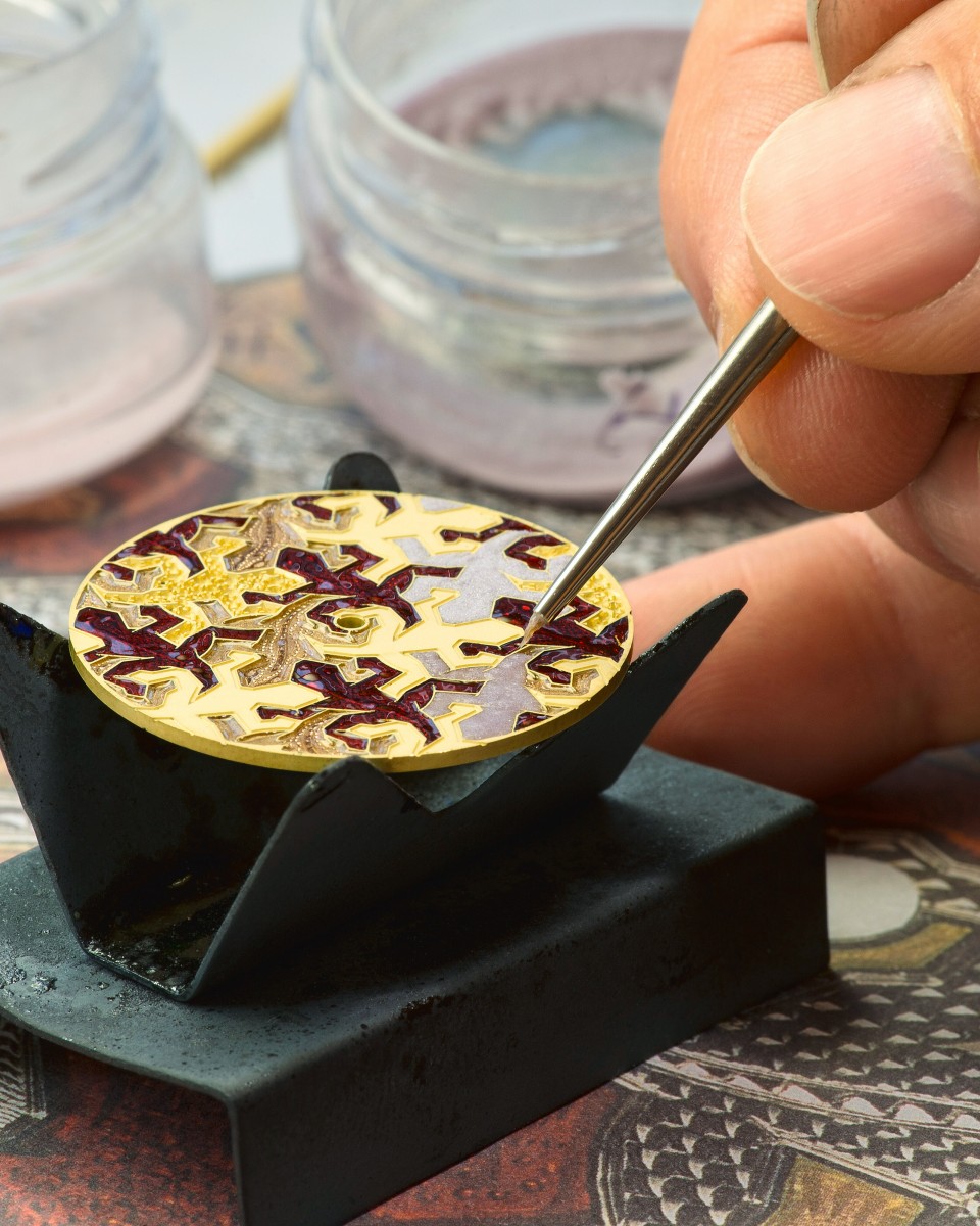  Artisan using a fine brush to apply enamel colors onto a patterned watch dial.
