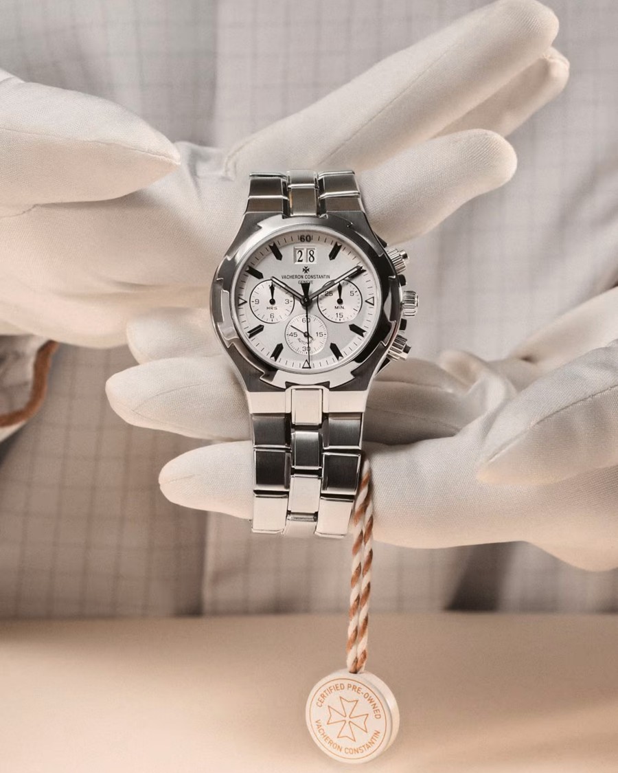 White-gloved hands hold a silver metal watch.