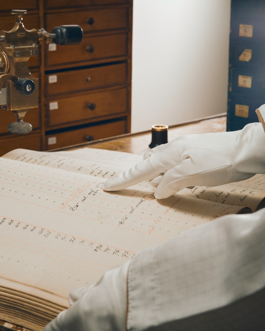 Hand in white gloves points to an entry in a notebook