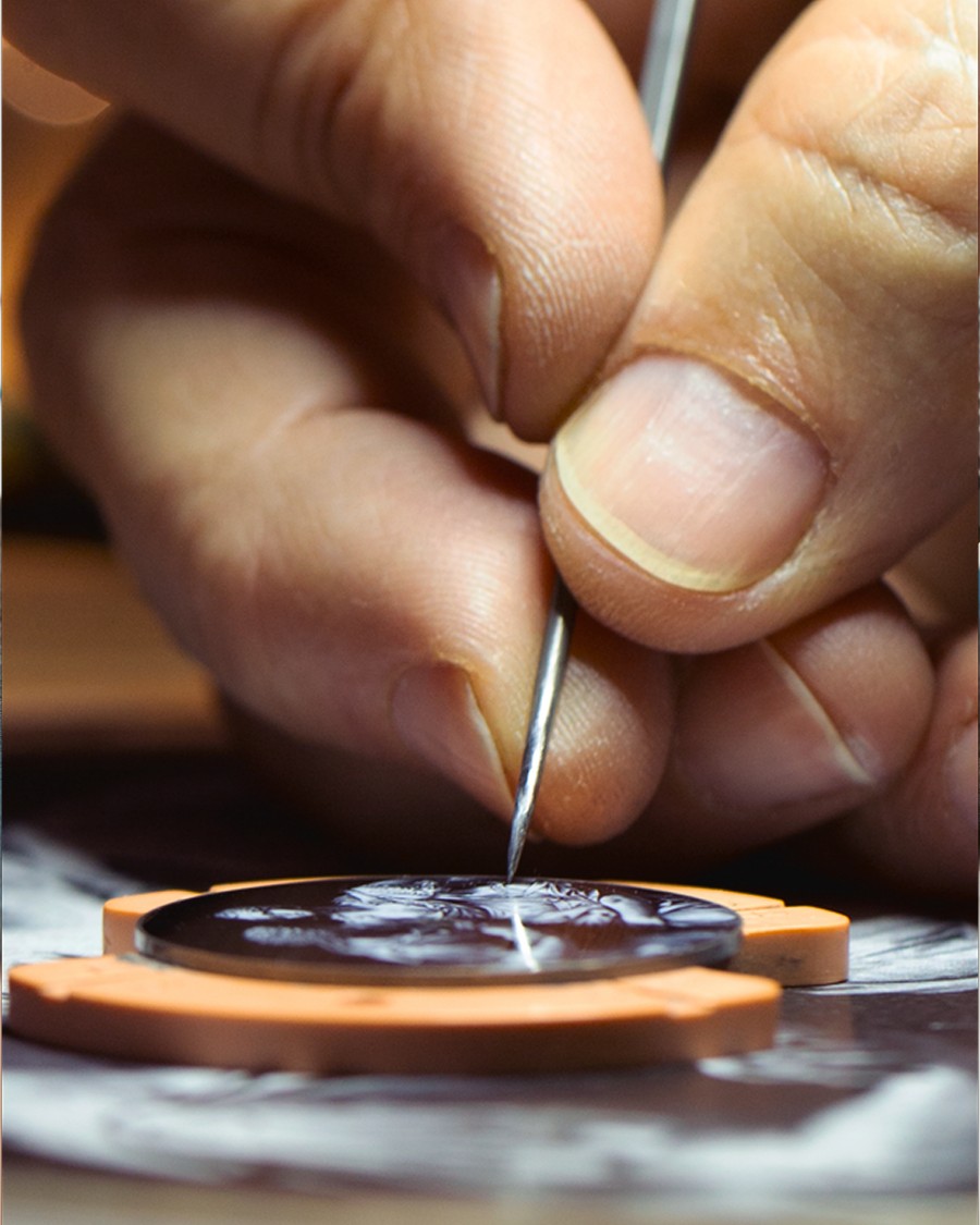 Close-up of a hand  engraving fine details into a watch dial with a precision tool.