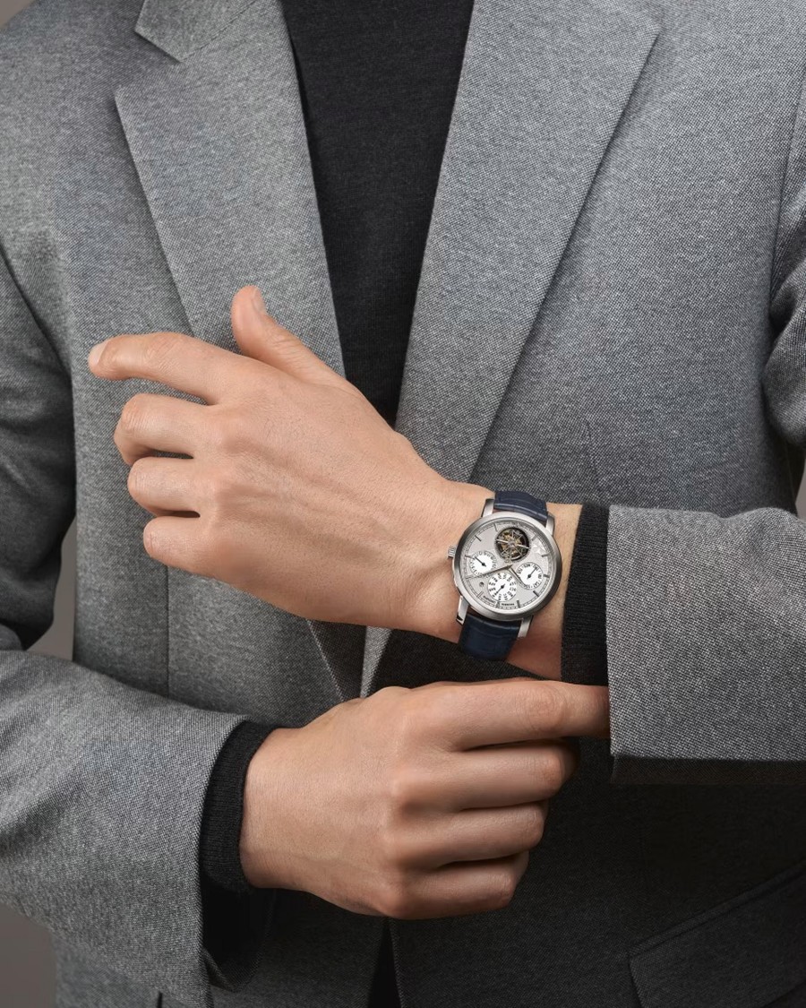 A stylish man in a grey blazer wearing a luxury watch with a tourbillon.