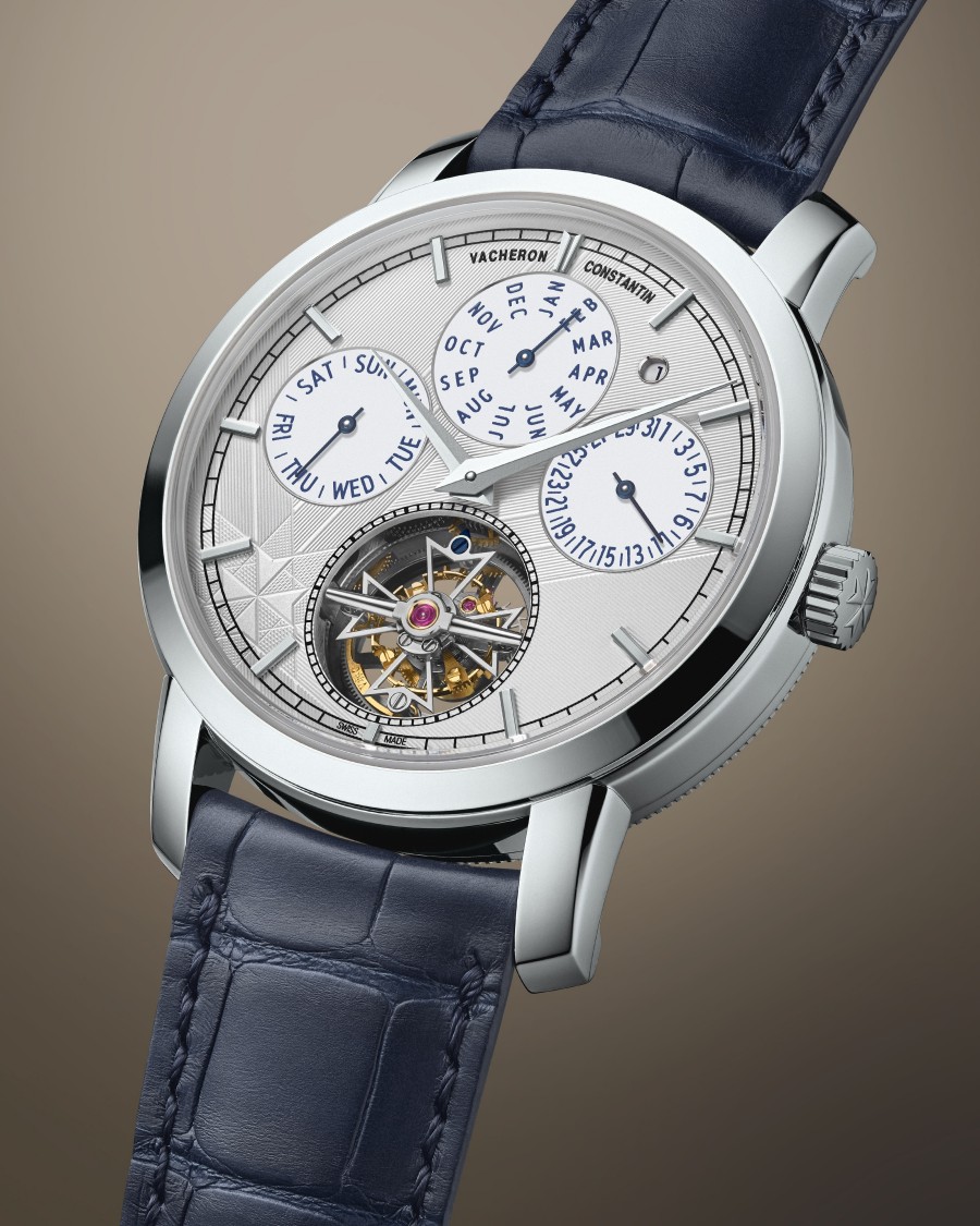 A watch with a blue leather strap, silver case, multiple calendar sub-dials, and an exposed mechanism.