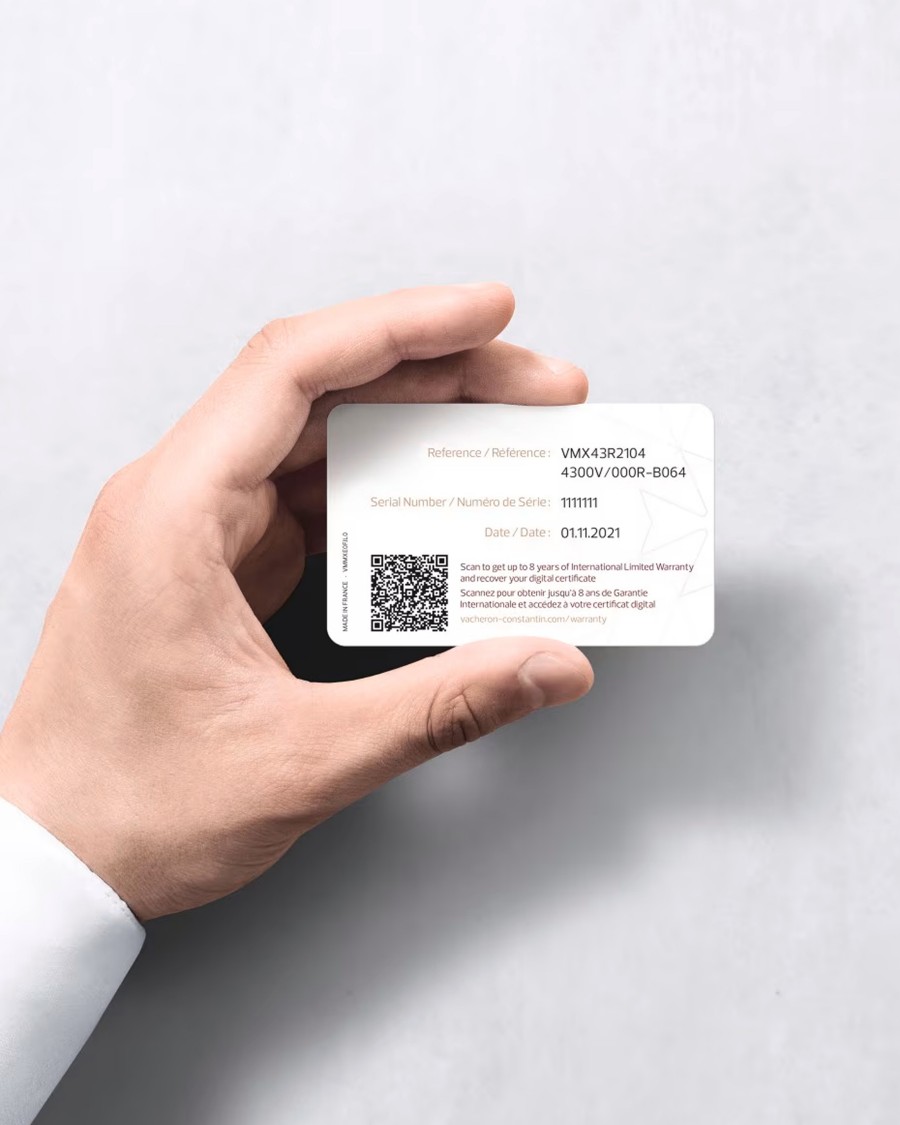 A hand holding a Vacheron Constantin white  warranty card with a QR code and typed details about the watch