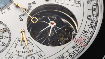 Close-up of  a watch dial showing calendar scales and a visible tourbillon.