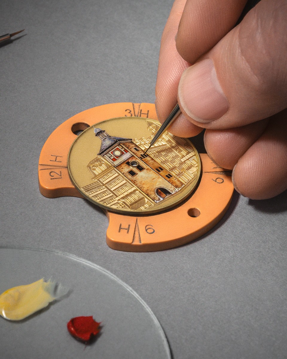 Artisan painting architectural details on a tellow watch dial using a fine brush.