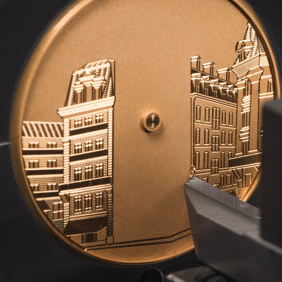 Engraving process of a gold watch dial depiciting historic buildings.