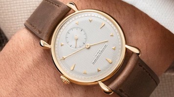 A man's wrist with a classy watch with golden details and a leather strap.