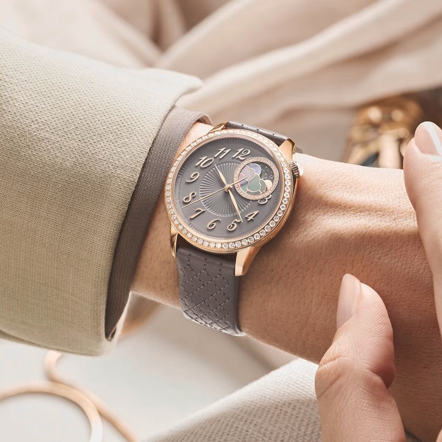 Close-up of a woman's hand in a light suit wearing a watch with a grayish leather strap and  a gold frame