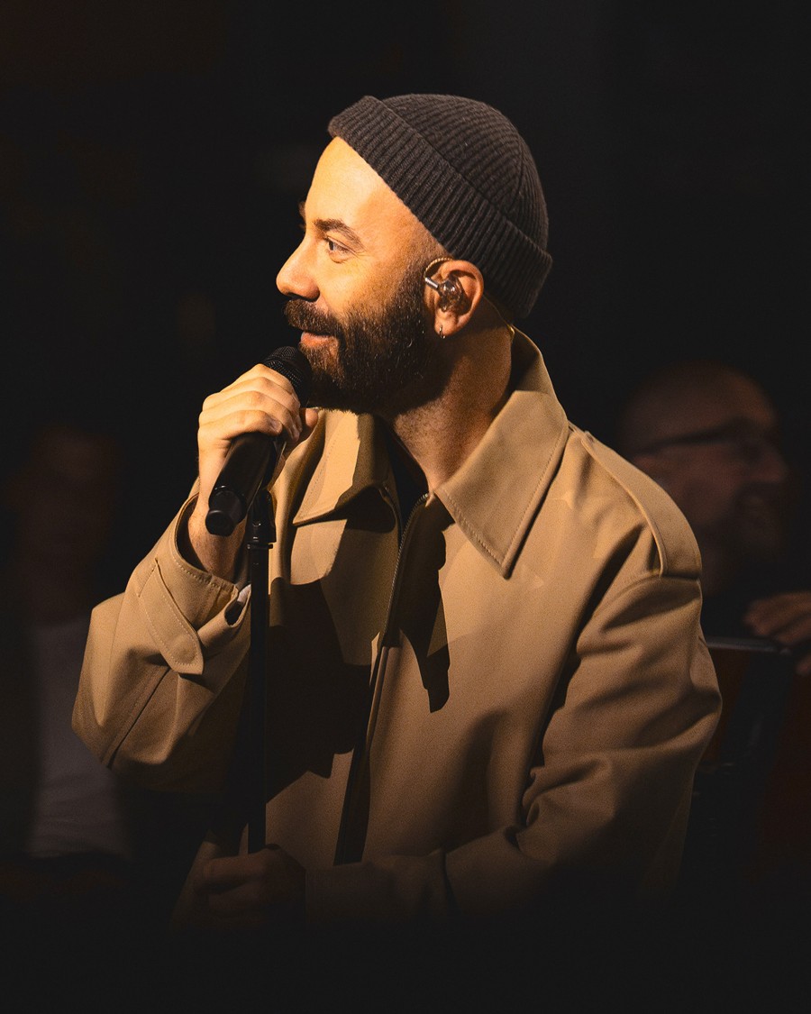 A man in a beige coat and black beanie holding a microphone
