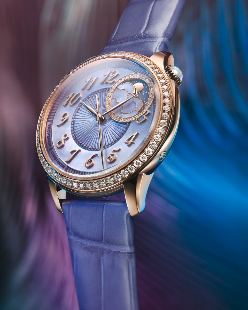 Close-up of a luxury wristwatch with a  moonphase and star motif against a rich blue background.