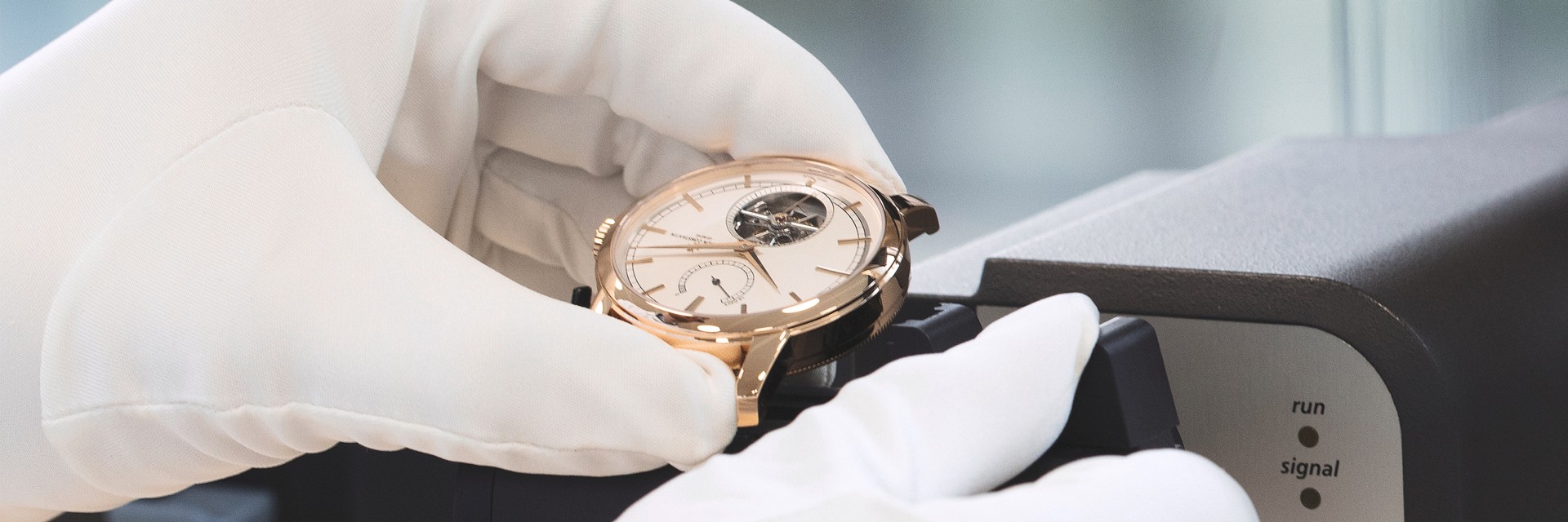 Gloved hands holding a Vacheron Constantin watch with an open case back, inspecting its intricate mechanical movement.