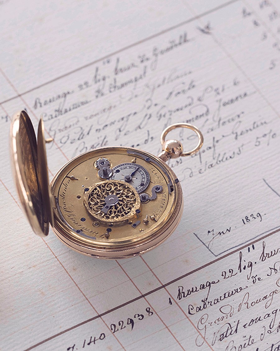 Open gold pocket watch revealing inner mechanical movement, placed  on handwritten documents.