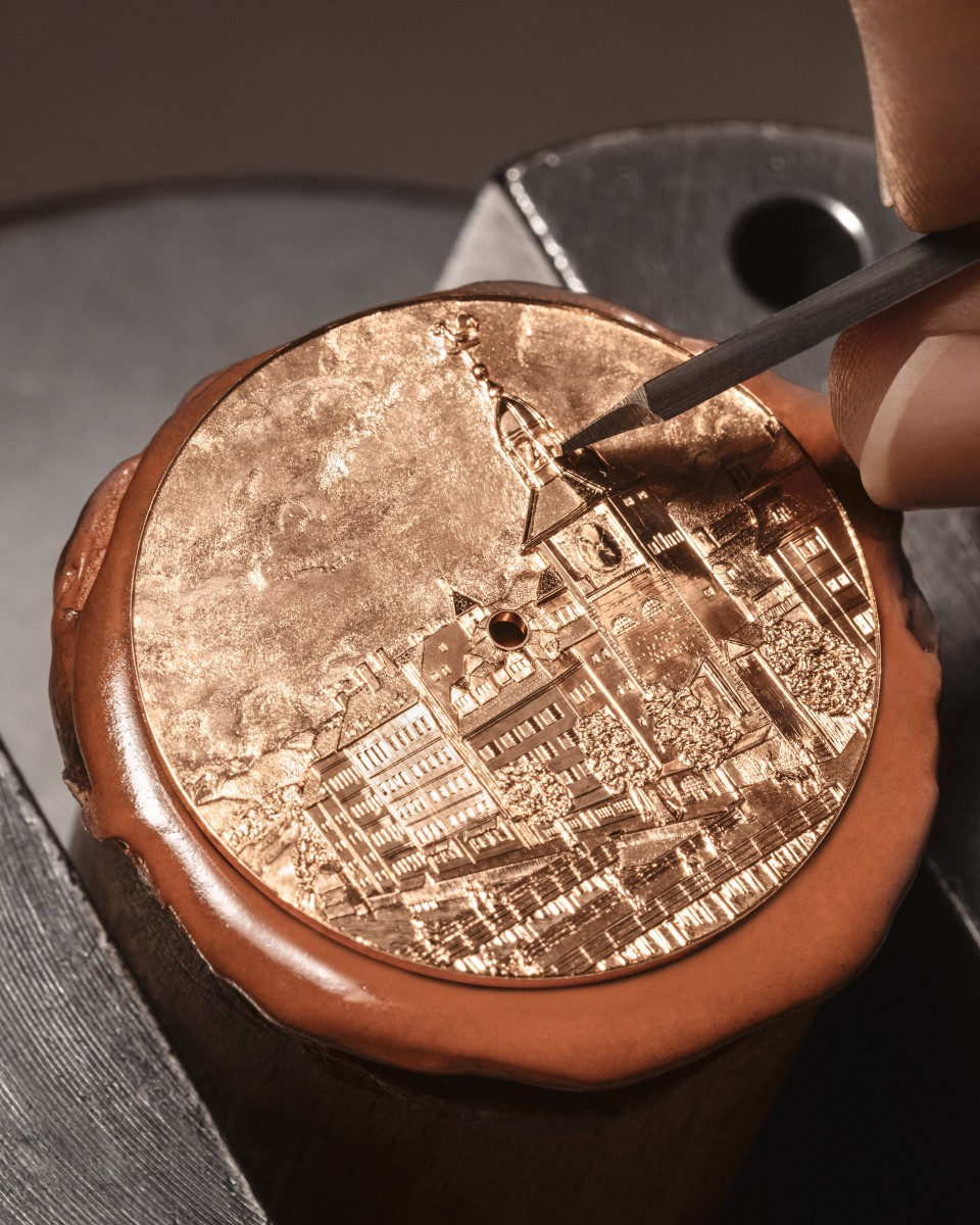 Close-up of a watch dial being hand-engraved with architectural motifs using a fine tool.