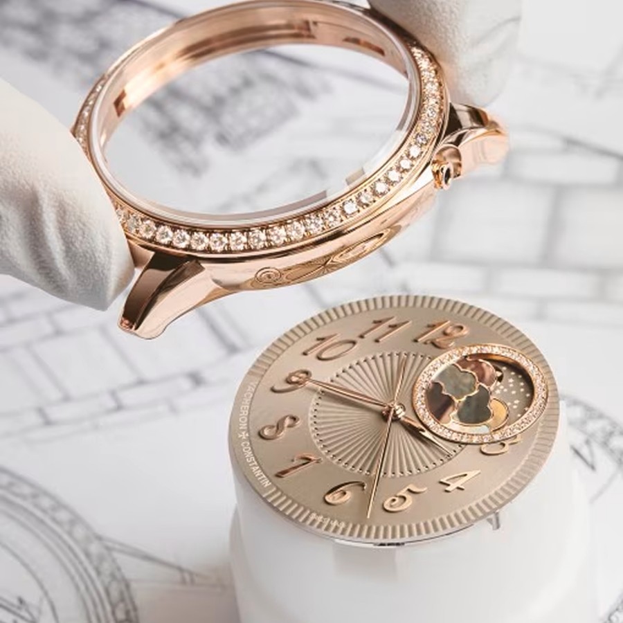 Close-up of a hand in white gloves placing a round gold watch bezel on a  case with a gold details