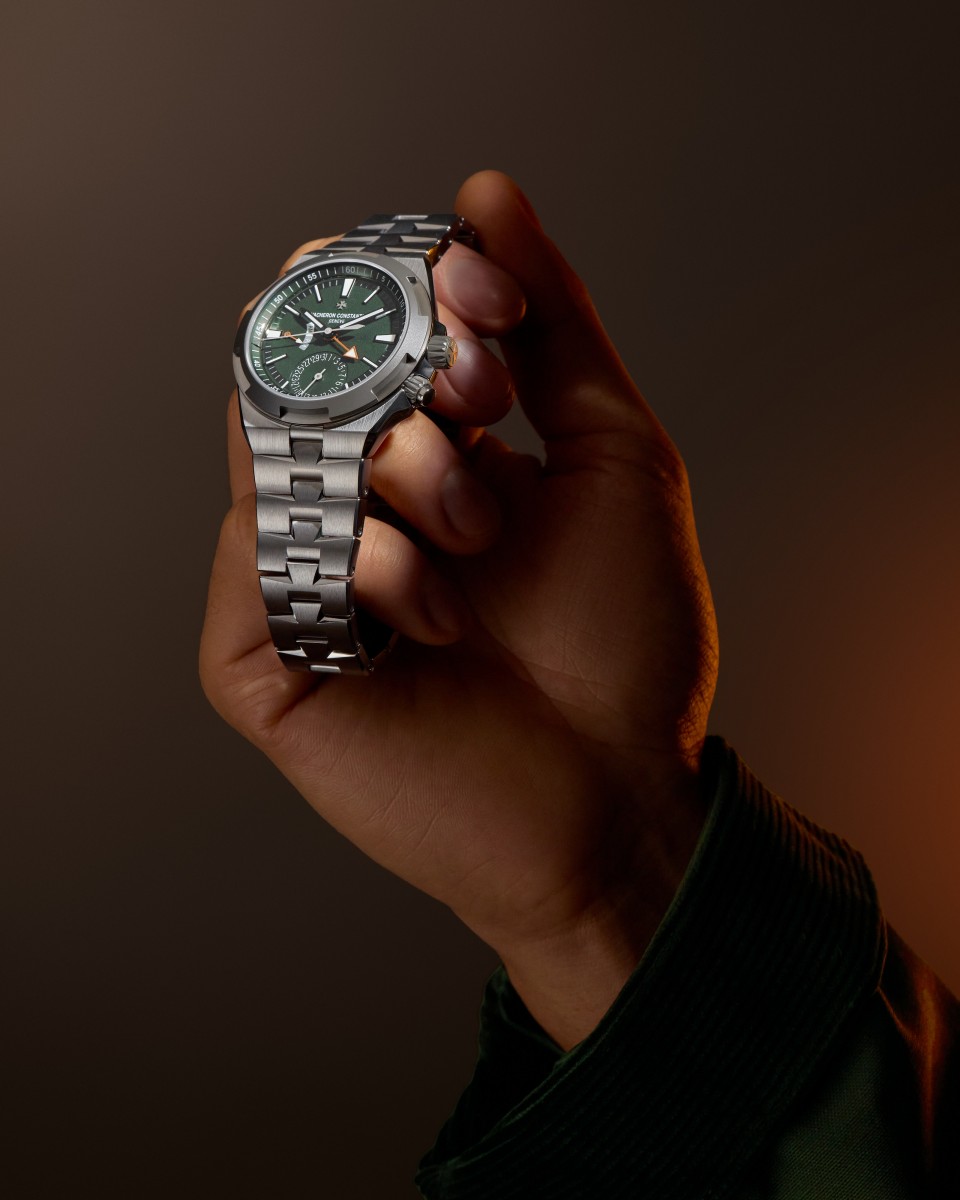 A hand holding Vacheron Constantin an Overseas dual time Cardinal Points watch with a metal bracelet.