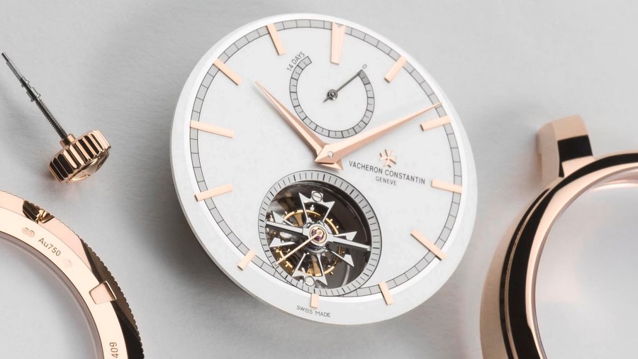 Close-up view of a watch case with light gray and gold elements and with a partially visible watch mechanism 