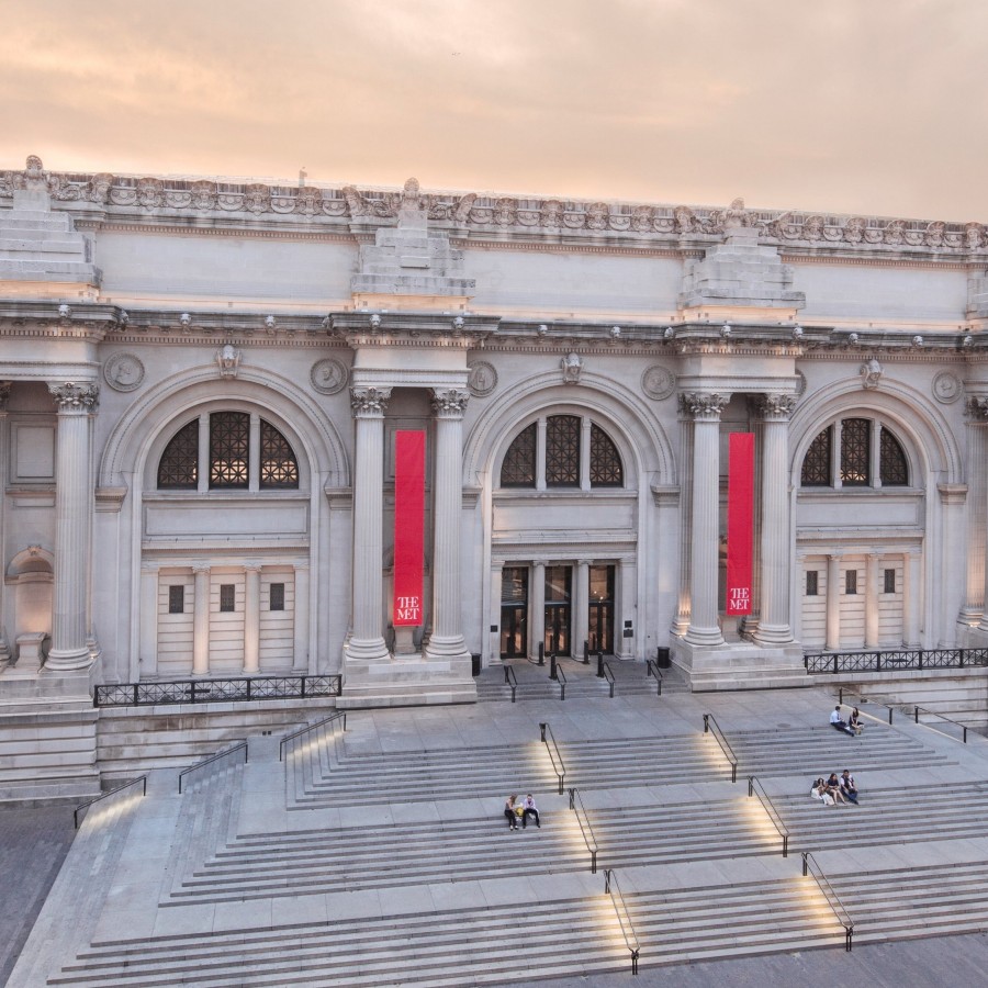 Exterion view of the Met museum with wide steps and  red  banners.