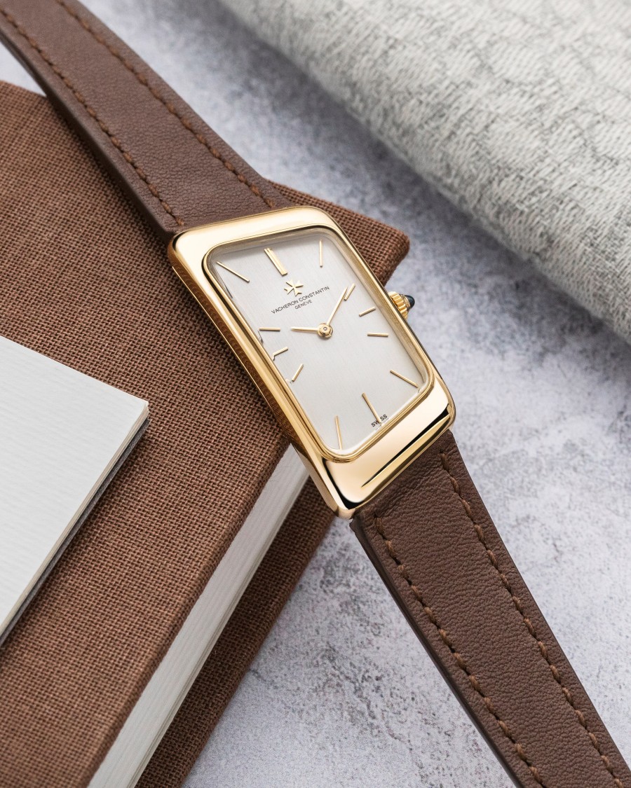 A watch with a square case, gold details, a light crystal, and a brown leather strap.