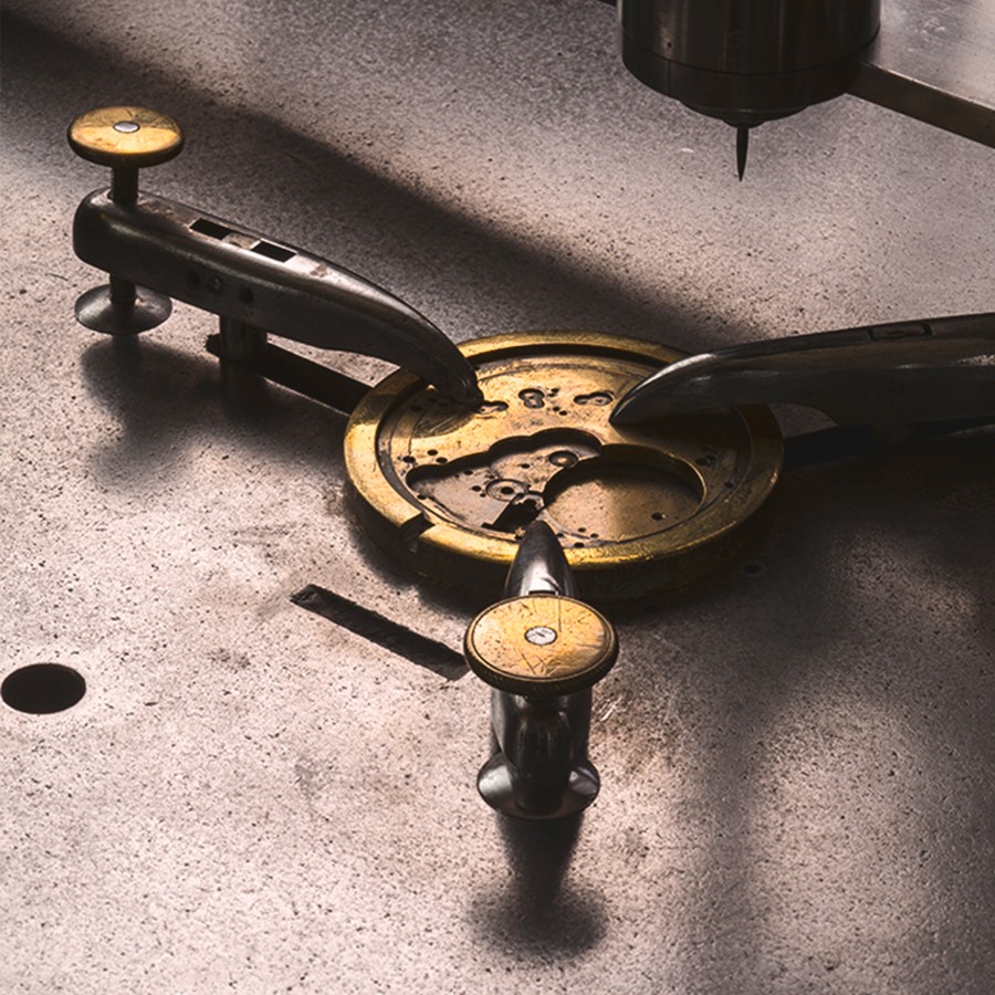 A golden watch movement is being worked on with tools.