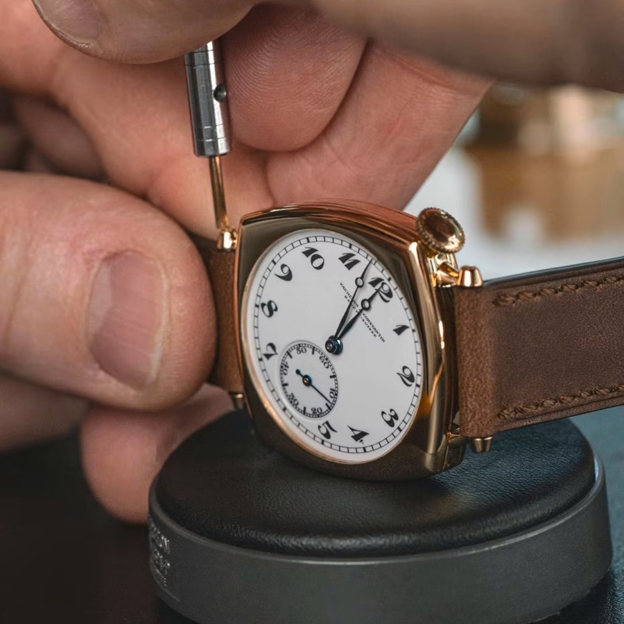 Close-up of a hand adjusting a Vacheron Constantin watch with a brown leather strap and white dial. 