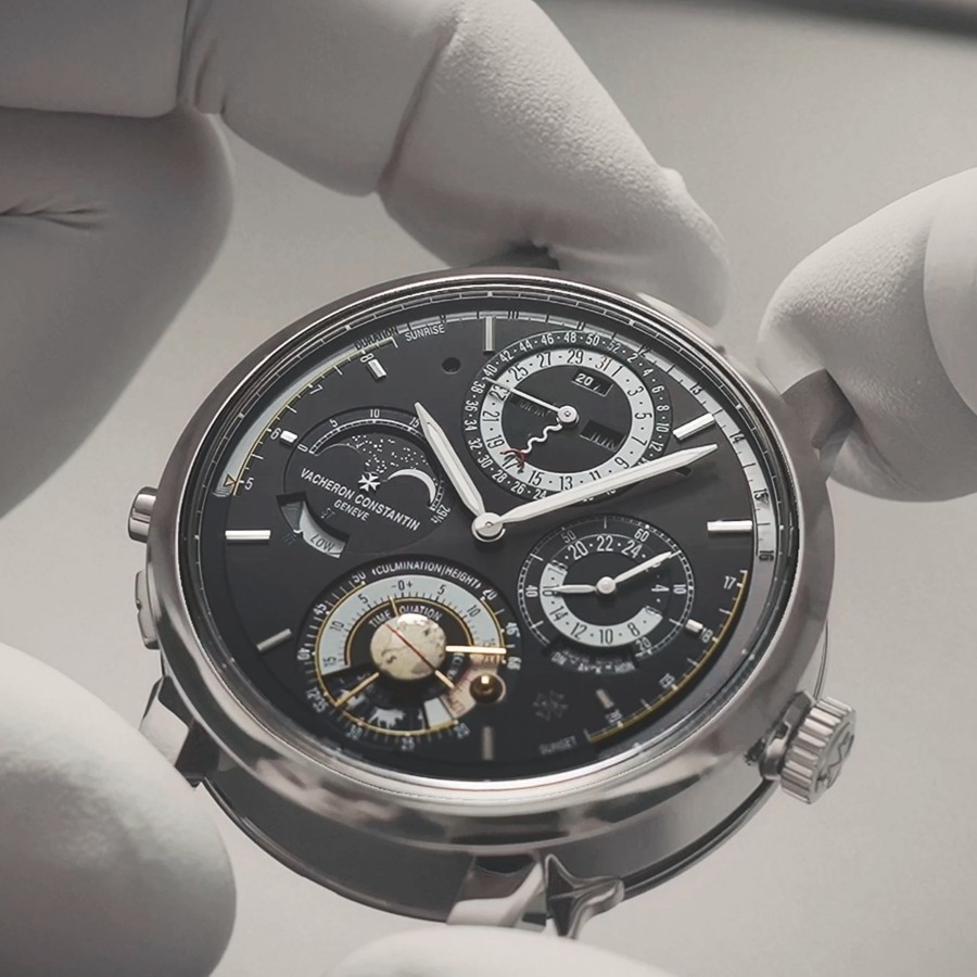 Hands hold the head of a watch with a black bezel and silver details
