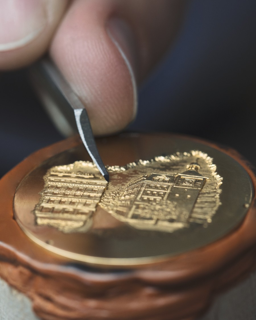 Close-up of  engraving in progress, depiciting buildings on a round metal piece.